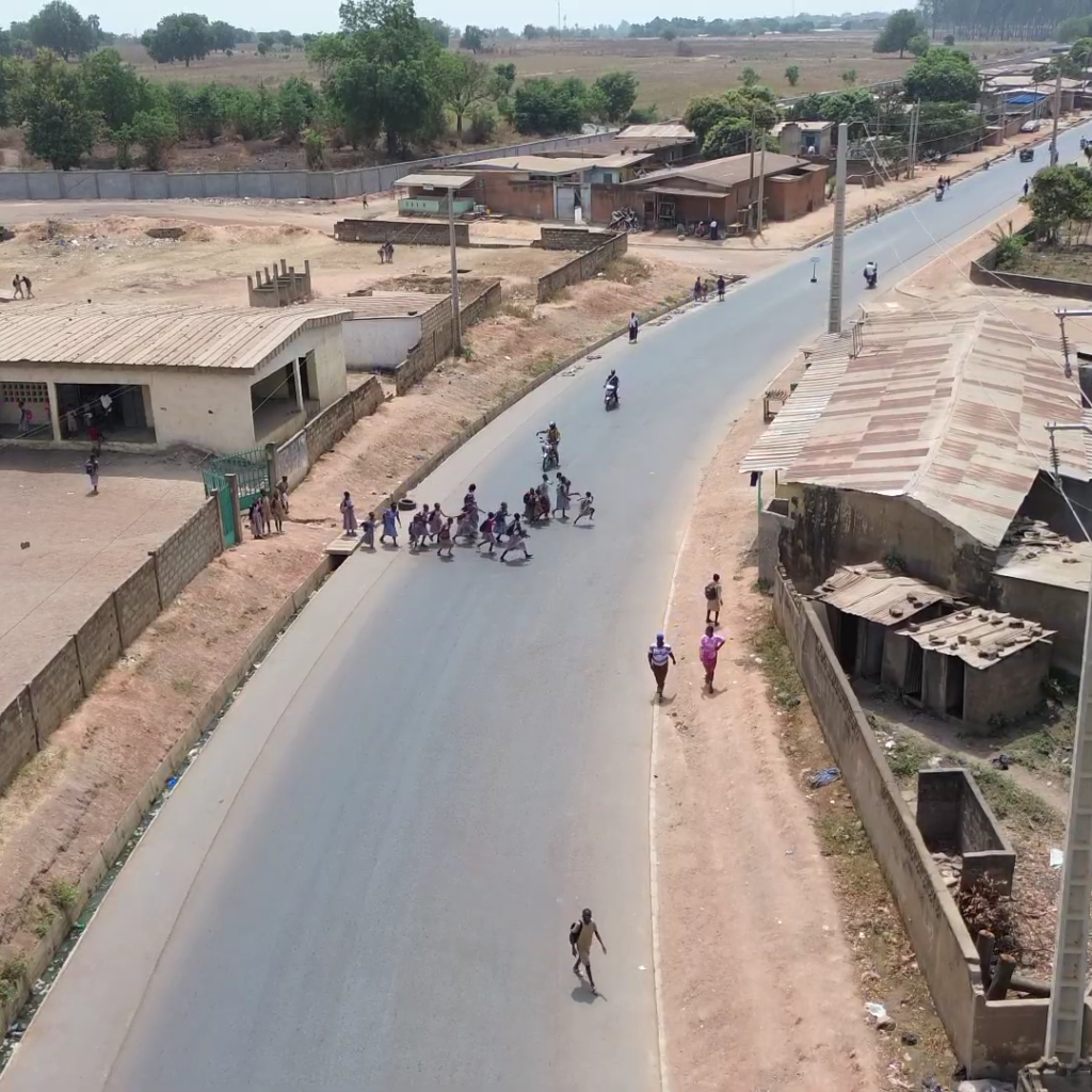 Drone view of a school gate with students trying to cross a recently asphalted road